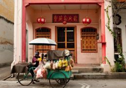 A food vendor walks past a traditional Chinese shopfront.