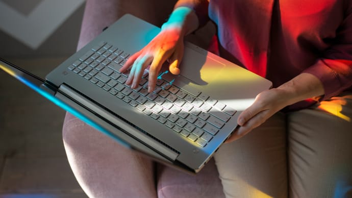 Hands typing on a laptop keyboard, illuminated by colorful light reflections.