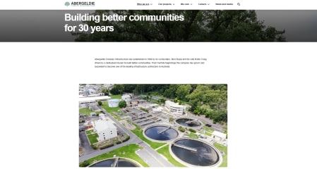 An aerial view of a water treatment plant with multiple circular tanks and buildings surrounded by green trees.